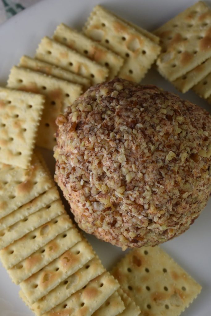 Cheese ball with blue cheese covered in nuts on a plate with crackers