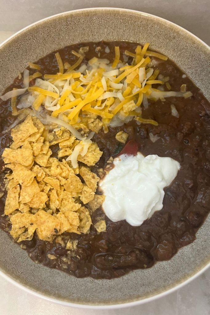 bowl of black bean soup with sour cream, corn chips and cheese