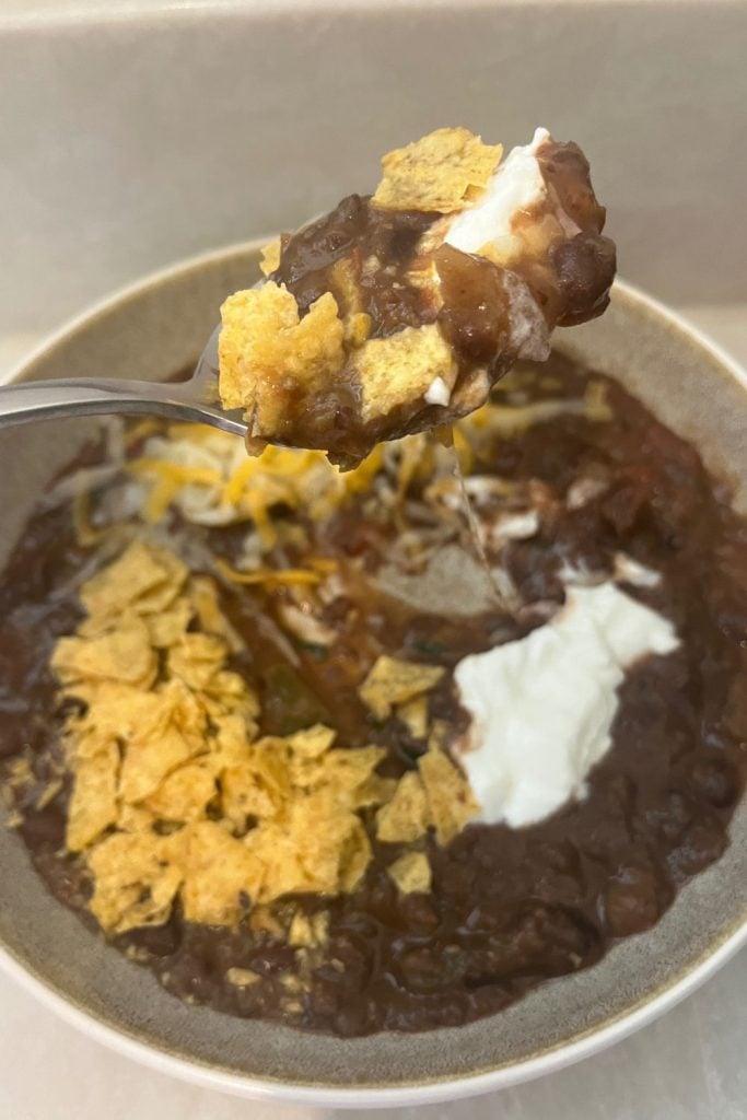 Spoon of black bean soup with crushed corn chips and sour cream