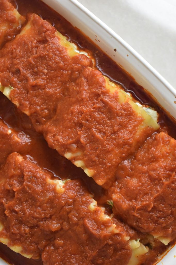 overhead shot of rolled up lasagna noodles stuffed with spinach ricotta filling topped with marinara sauce